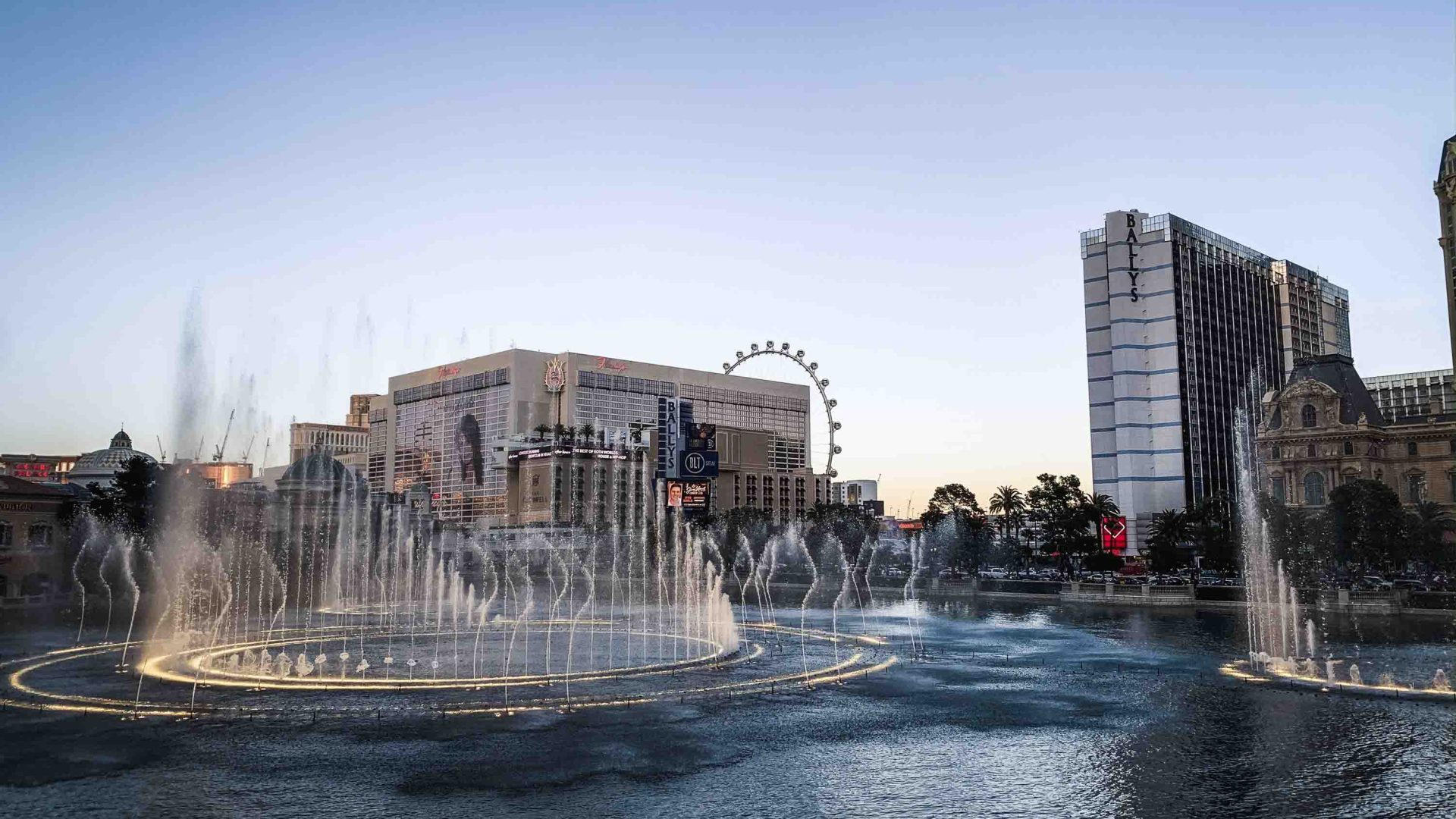 A large, modern hotel in Vegas with a circular water fountain in the foreground.