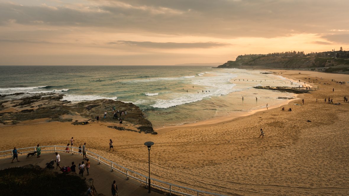 People walk along Newcastle Beach in New South Wales, Australia, at sunset.