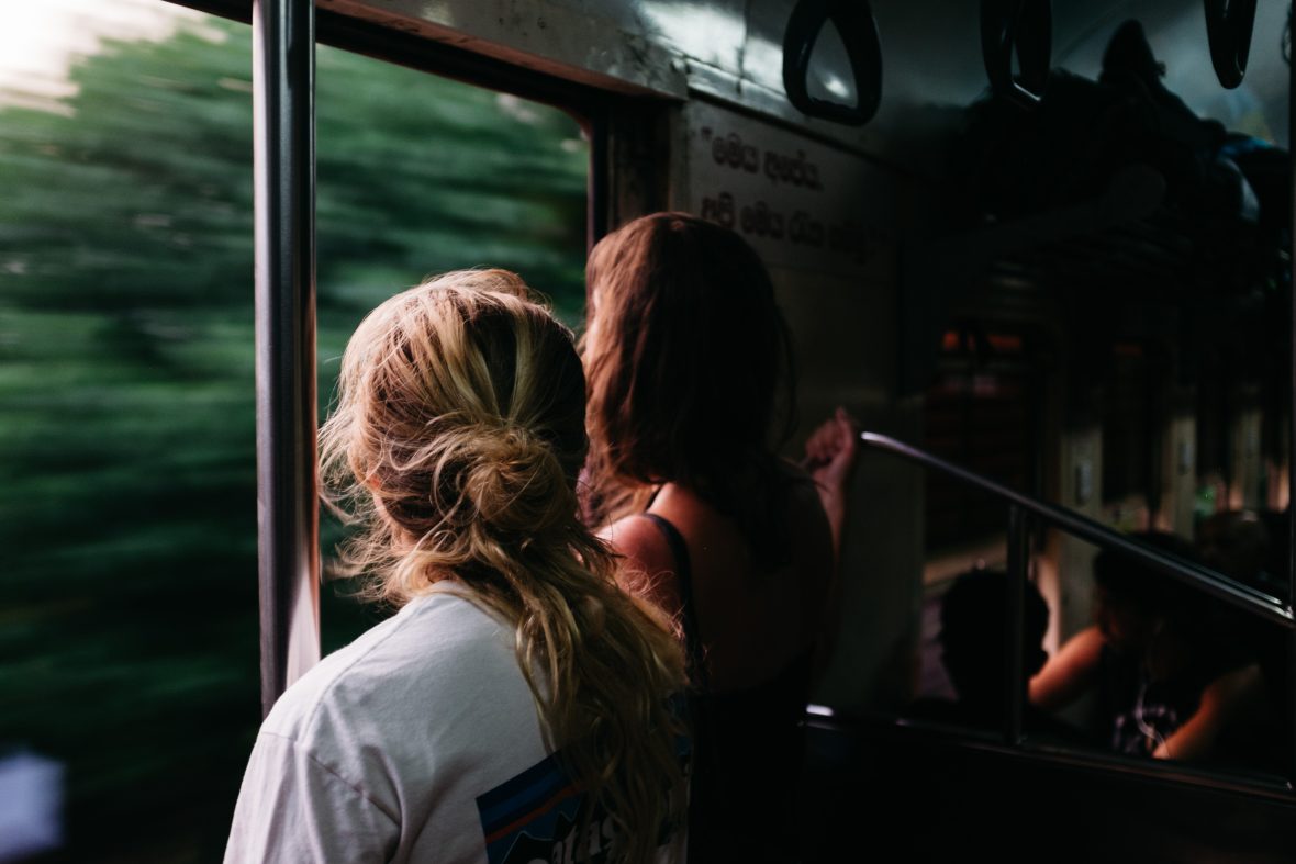 Two women look out the window of a fast-moving train at the greenery sweeping by.