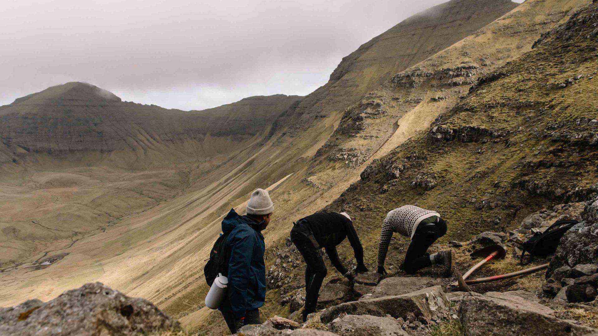 Three people are bent over working in the mountains.