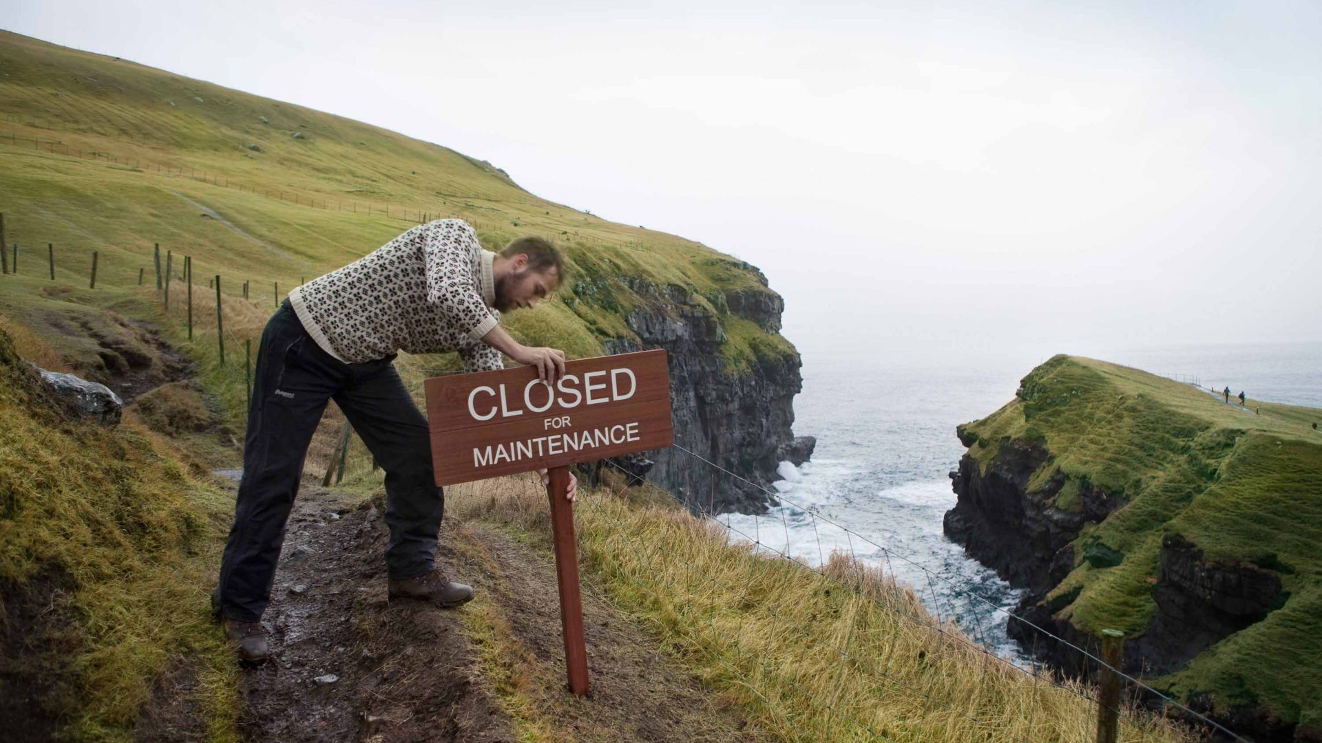 A man pushes a Closed for Maintenance sign into the ground.