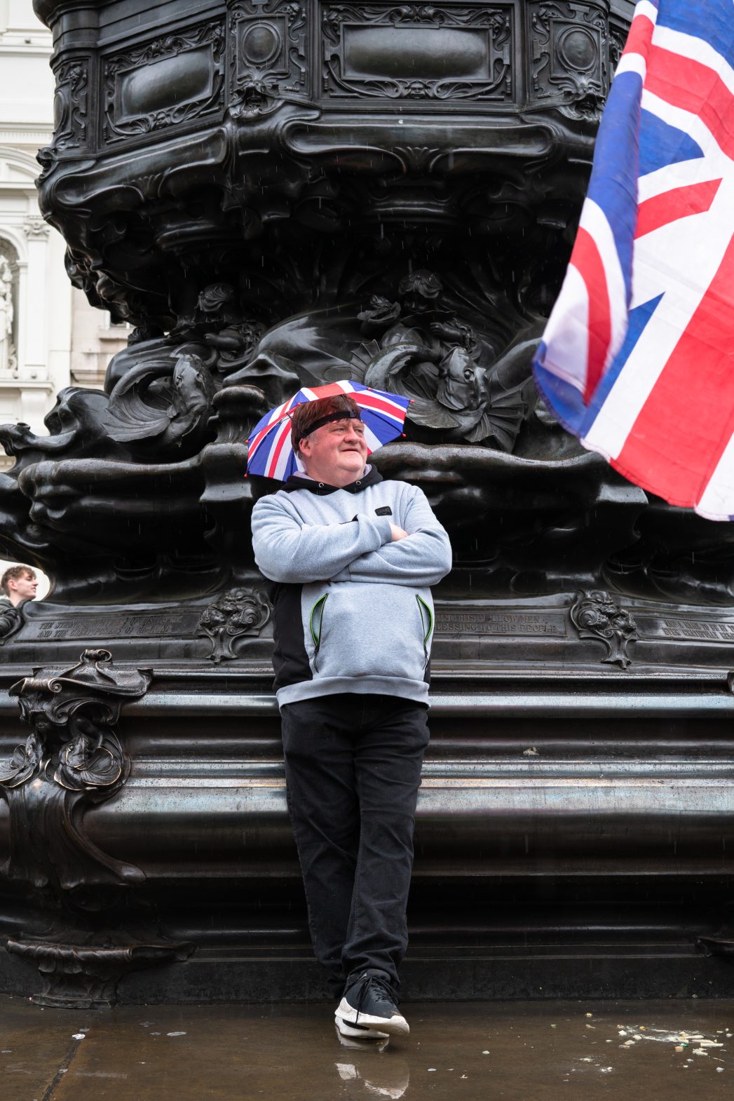 A man stood against a statue wearing a Union Jack umbrella hat.