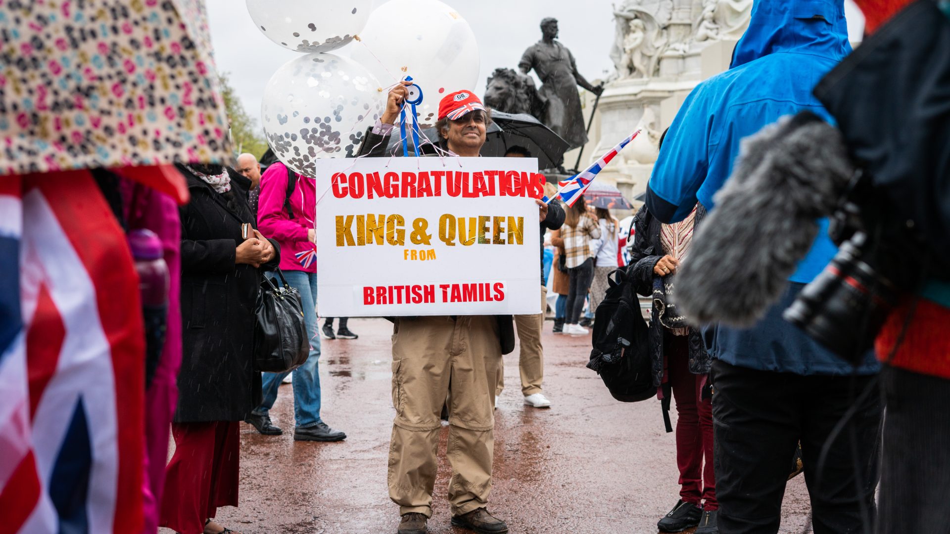 A man holds up a sign saying 'Congratulations King & Queen from British Tamils'.