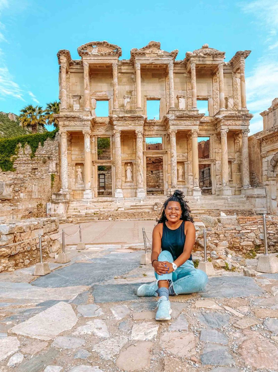 A black woman sits on the ground in front of some ruins.