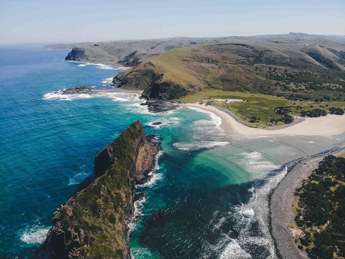 An aerial view over the green hills and aquamarine ocean of South Africa's eastern coastline.
