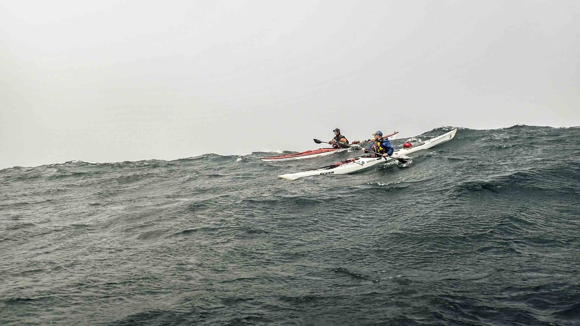 Two people kayak on waves.