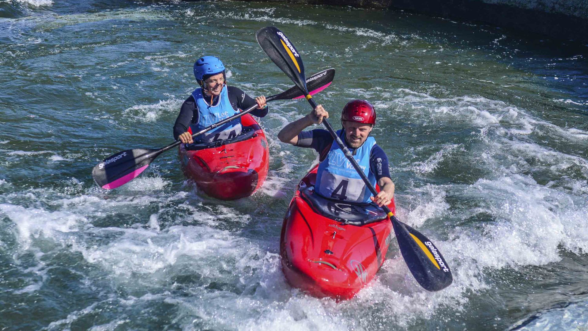 Two people smile and laugh as they kayak through the water.