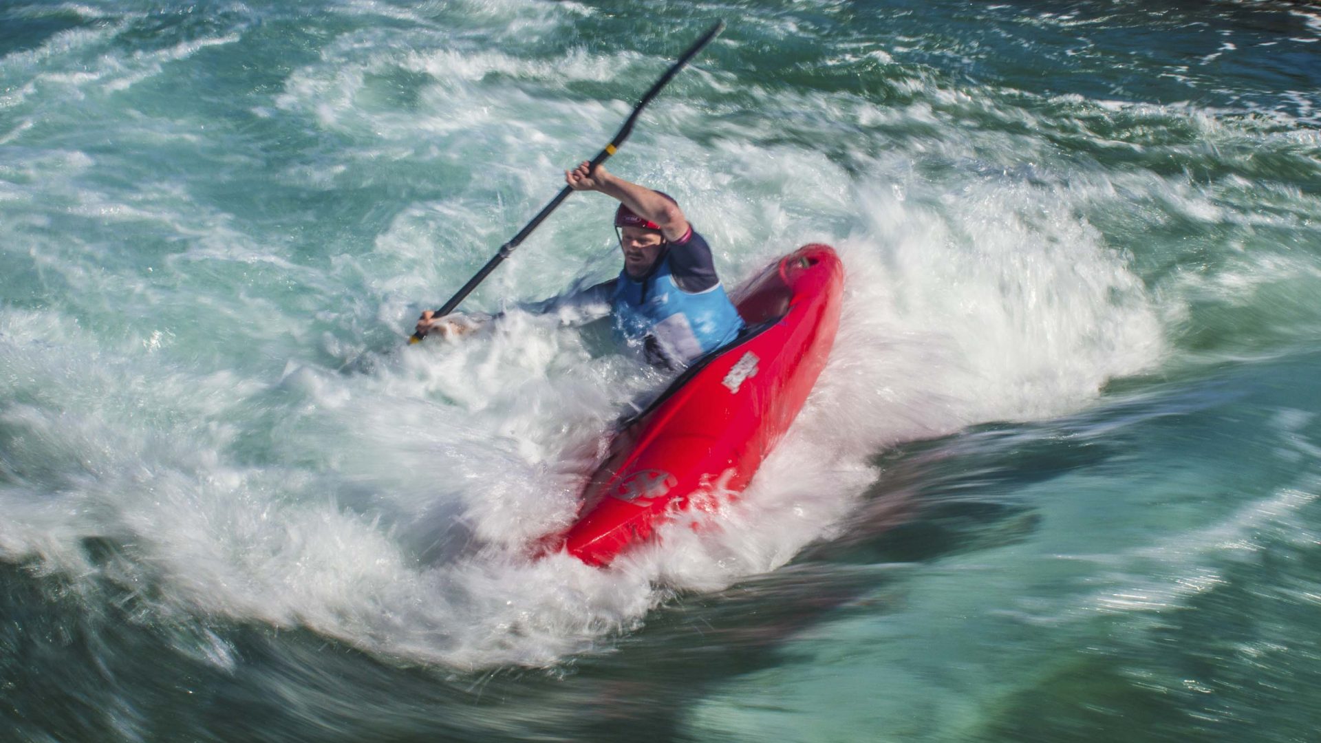 A man in a red kayak goes through white wash.
