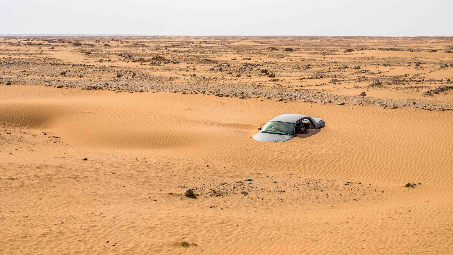 A car sinks underneath the sand in the desert.
