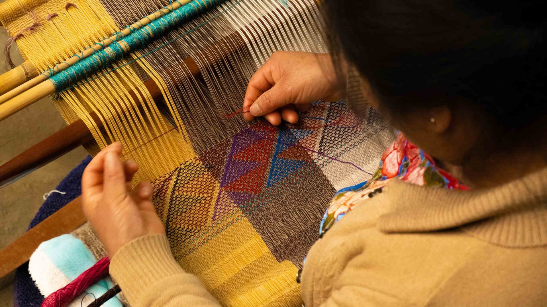 A person uses a loom to sew a colorful garment.
