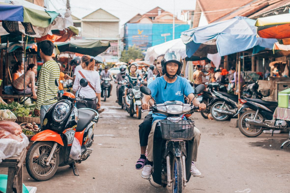 People on scooters ride through the centre of a market.