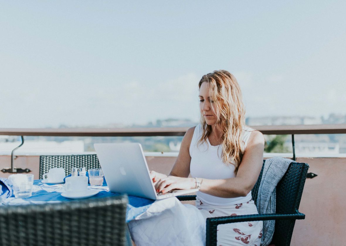 A woman works on her laptop at a cafe table overlooking a city.
