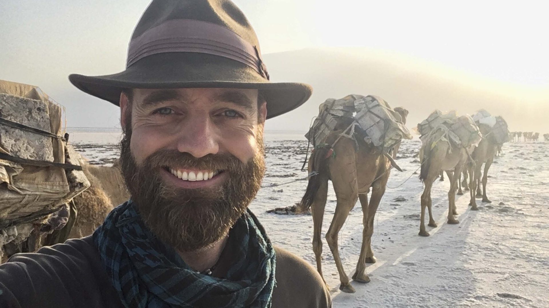 A selfie of Thor in the foreground with camels walking behind him in the background.