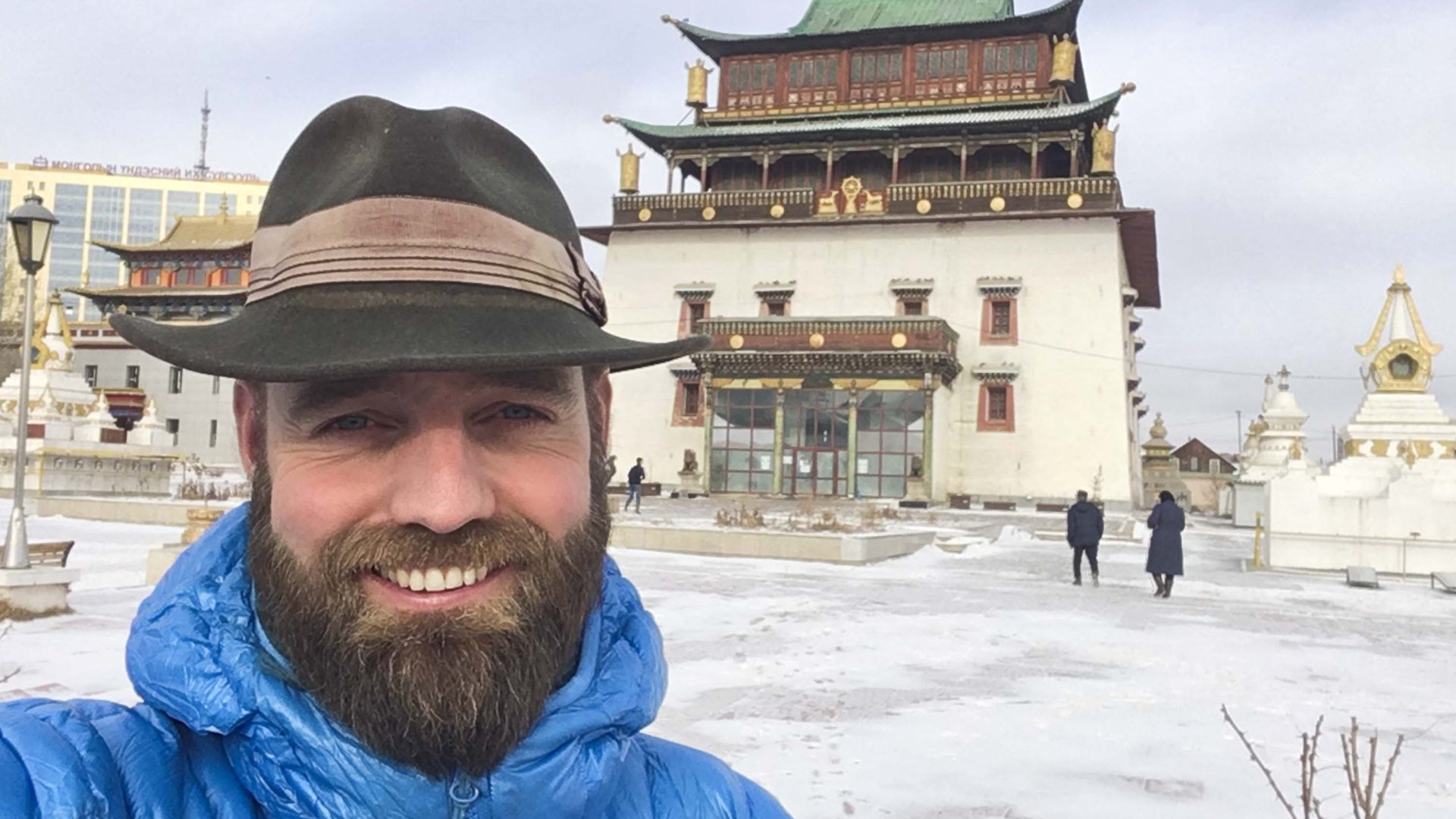 Thor in front of a temple with white walls and green roof in Mongolia.