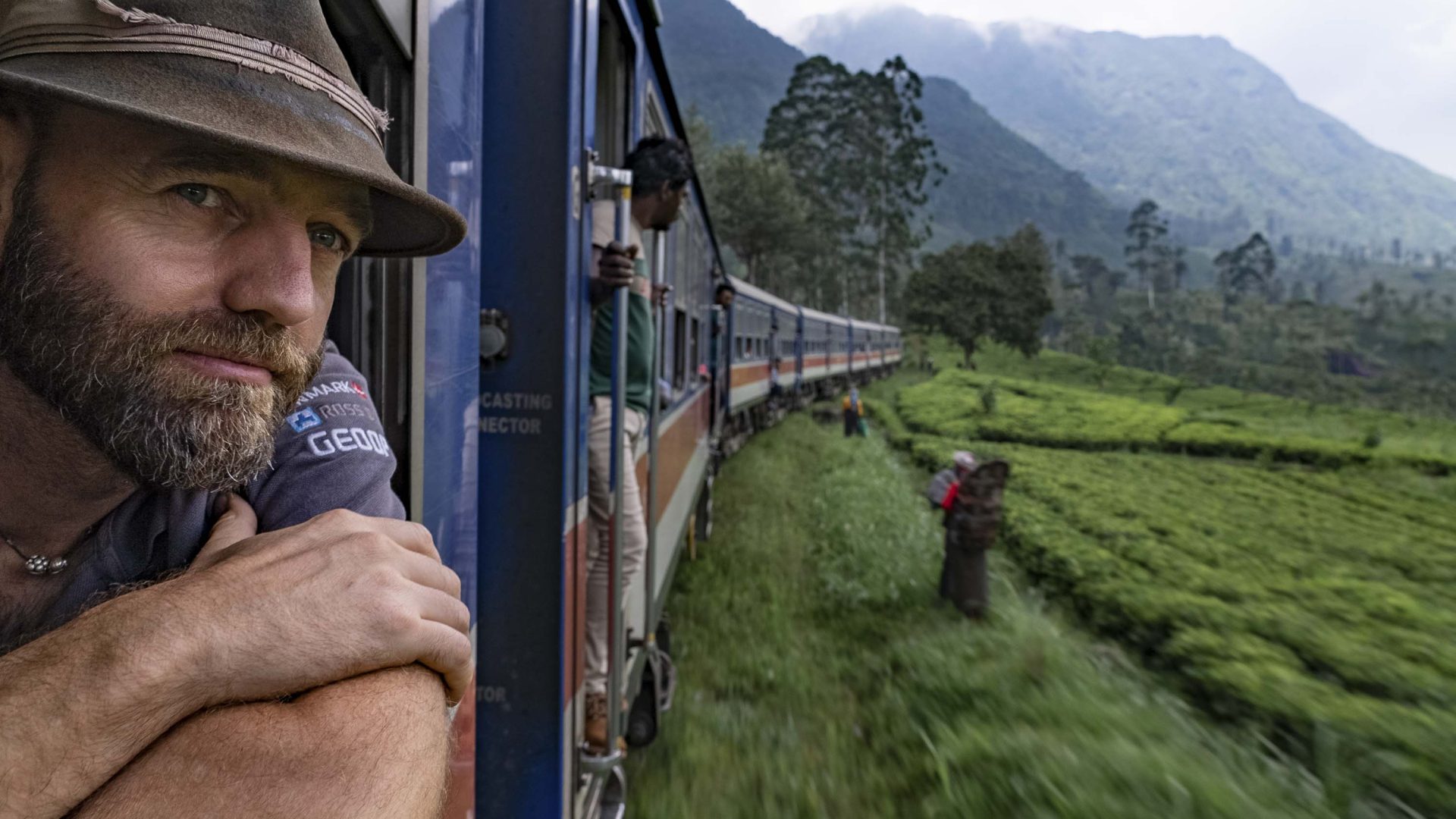 Thor looking out the window of a train in Sri Lanka at green fields and mountains.