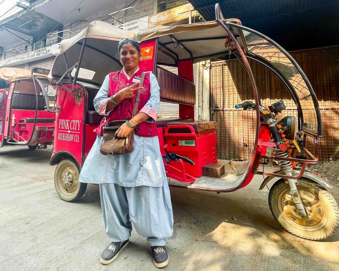 Renu gives a peace sign in front of the rickshaw she drives for Pink City rickshaws.