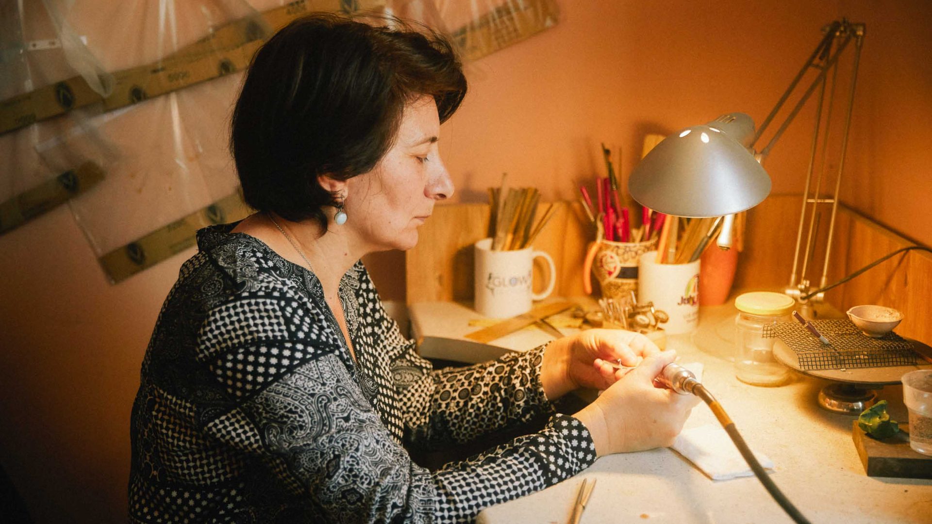 A woman works at a desk making jewellery.