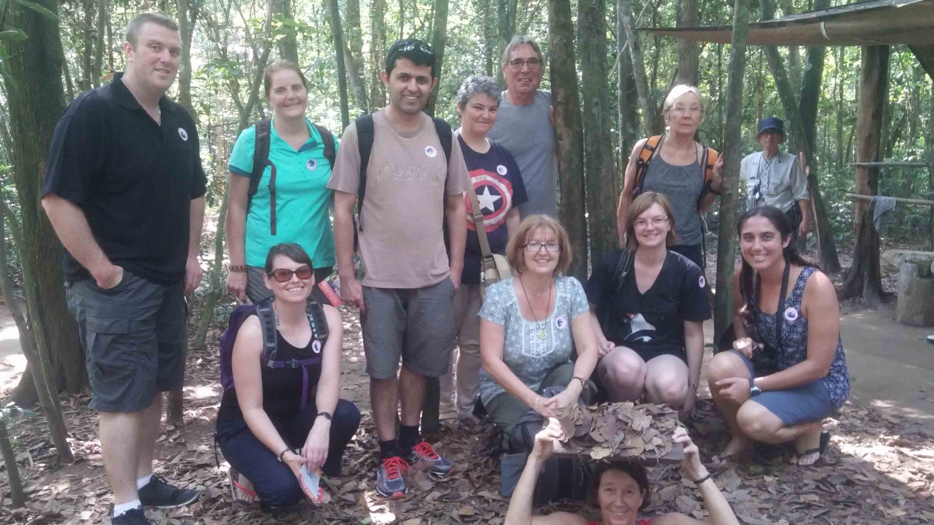 A group of people smile at the Cu Chi tunnels.