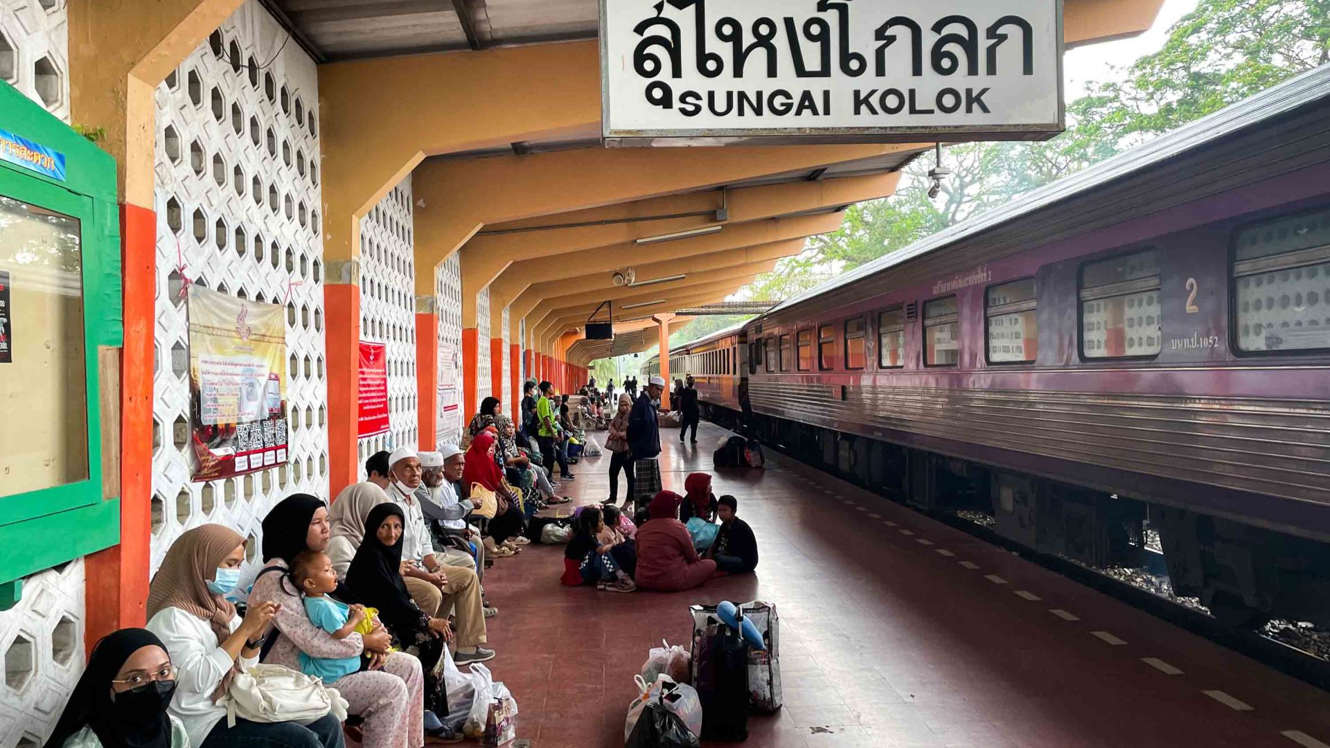 People sit on the platform of a station with a train pulled in.