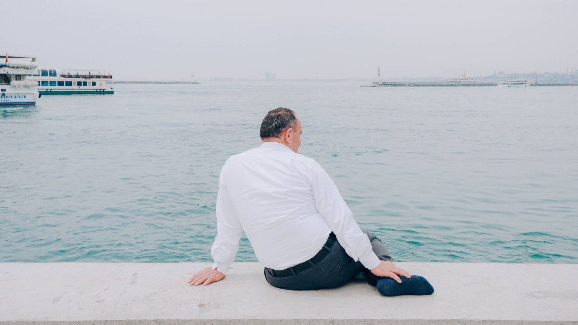 A man in a white shirt and black trousers looks out at the water.
