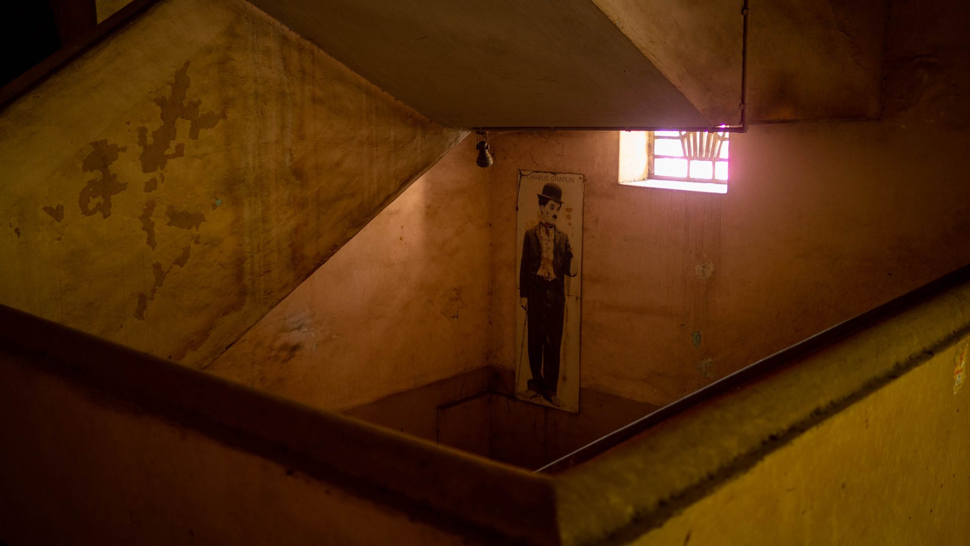 An old image of Charlie Chaplin on a wall of old yellowing paint in a stairwell.