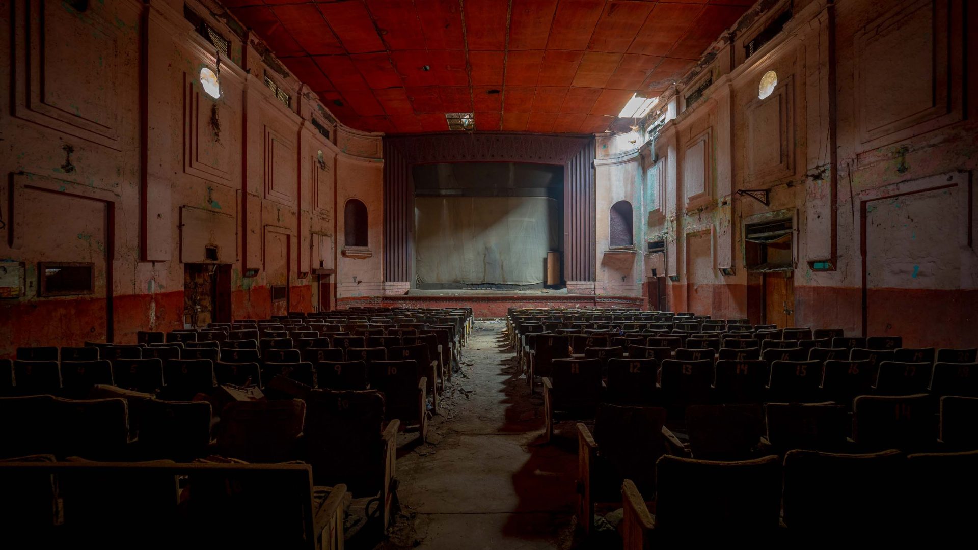 The interior of an abandoned cinema which is decorated and painted in red tones.