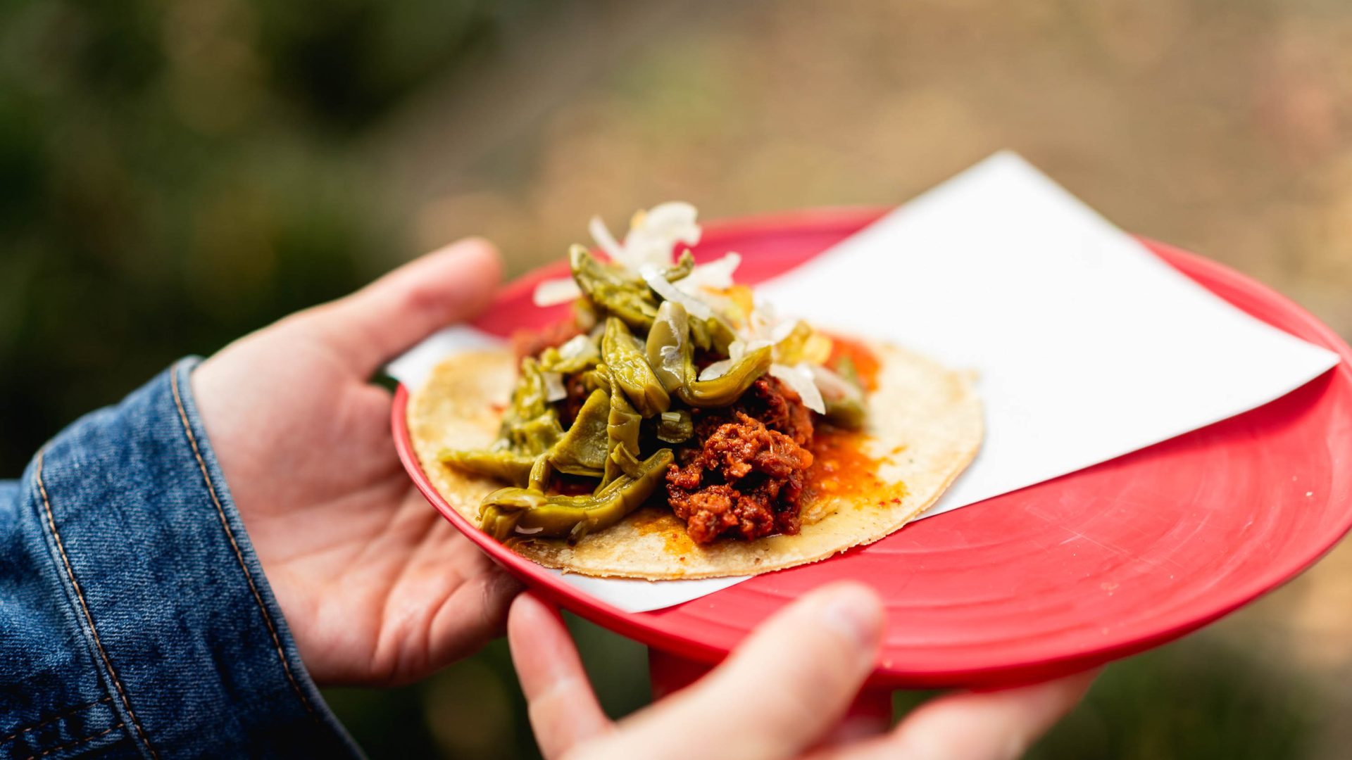 A hand holds a red plate with a Mixiote taco.
