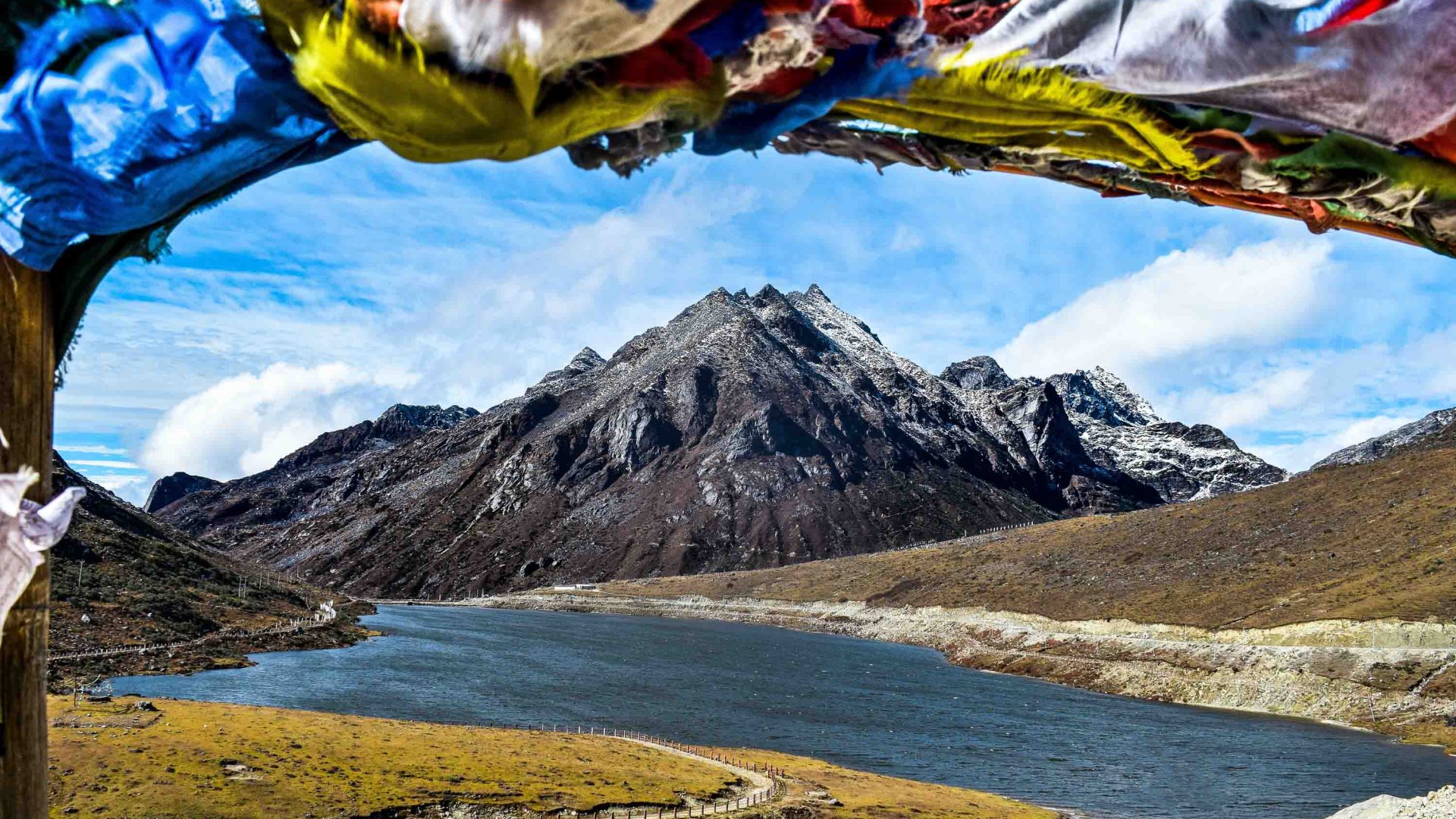 Prayer flags frame a stunning vista of blue lake and snow capped mountains.