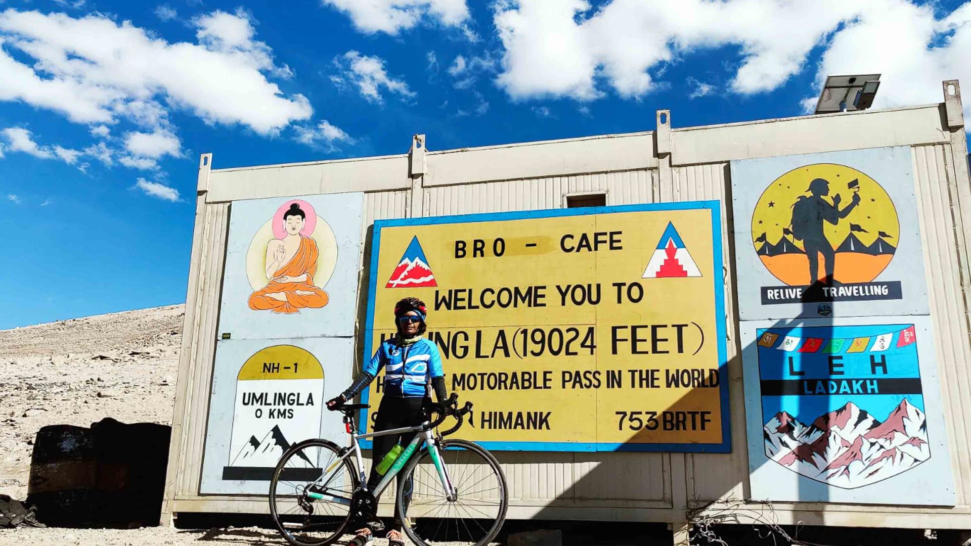 Preeti stands with her bike in front of a sign for Umling la Pass.