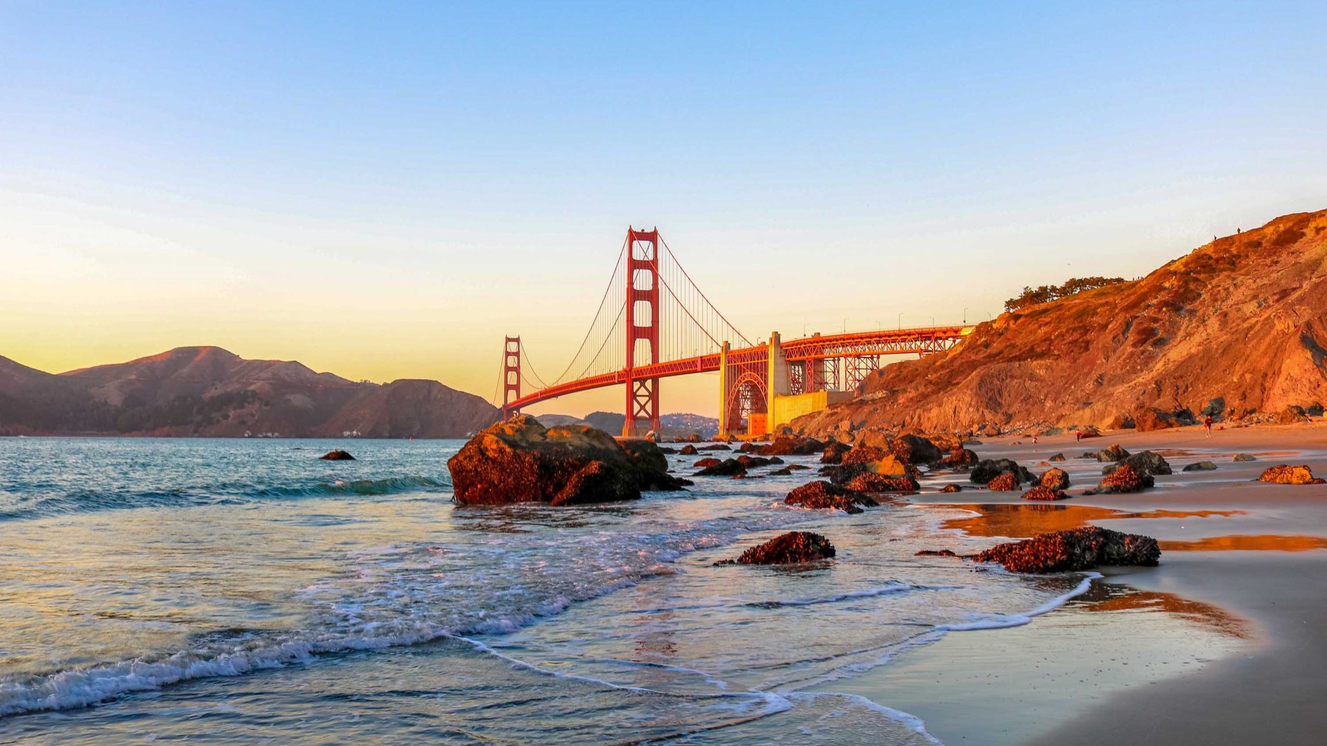 A beach leads to the Golden Gate Bridge at sunset.