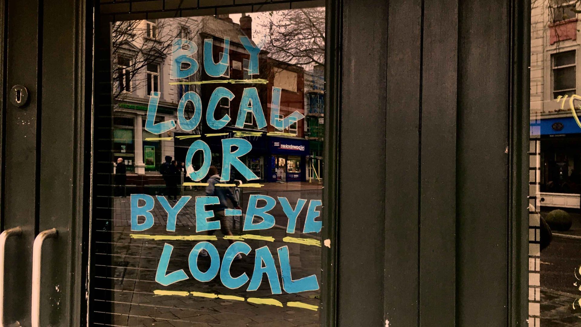 A sign in the front of a business reads "Buy local or bye bye local".