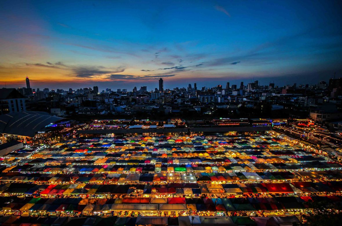 A night market with colorful tents and lights in the foreground and the city in the background.