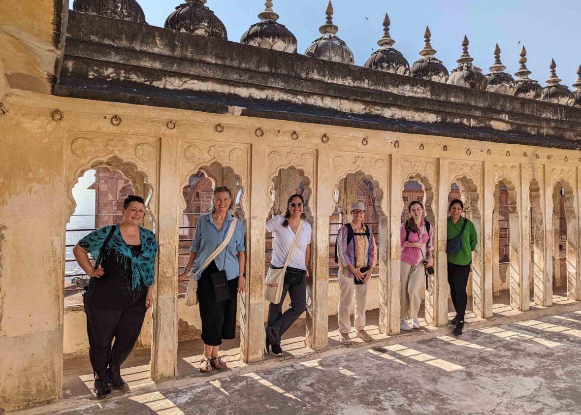 A group of women each stand under a small arch at a fort.