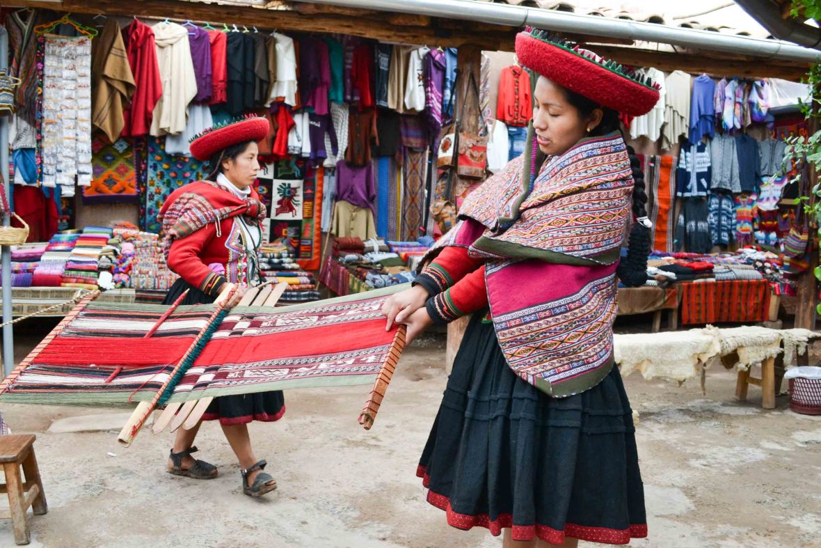 Two women in traditional Peruvian clothing weave.