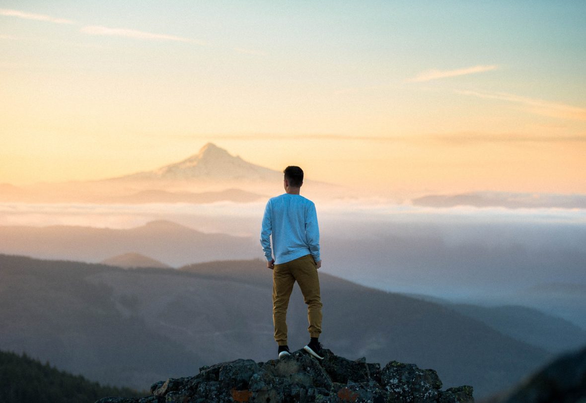 A man looks out at some mountains at sunset.