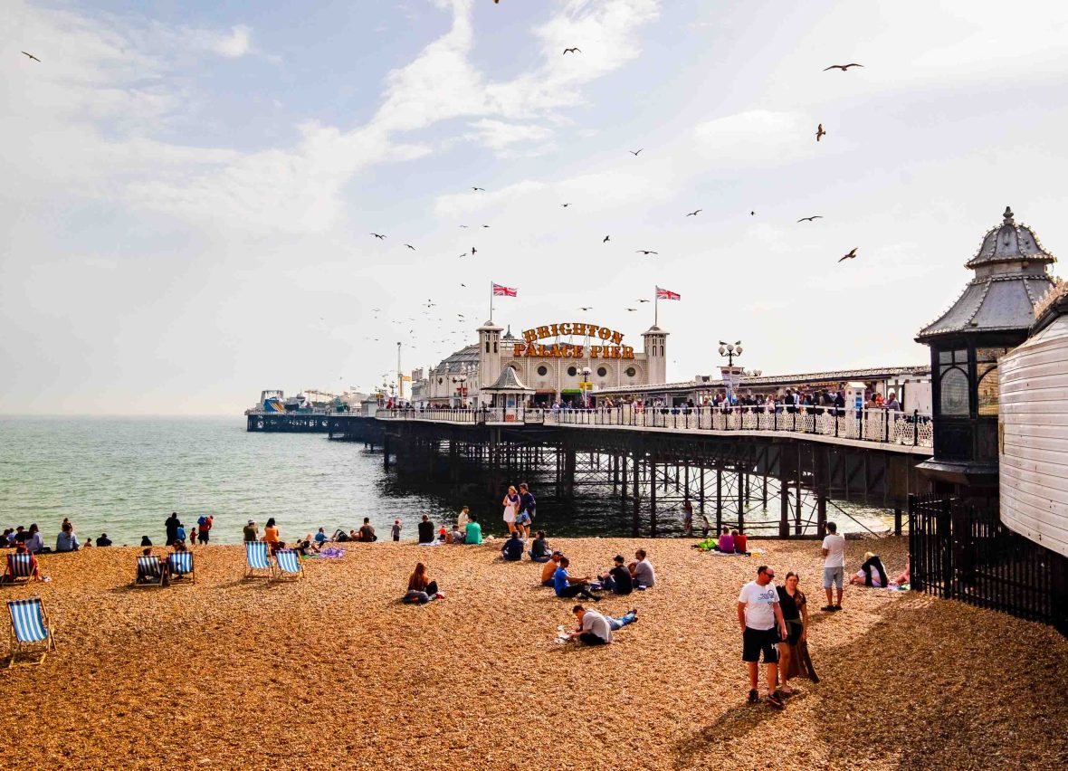 People sit on a beach, with Brighton Pier on the right.