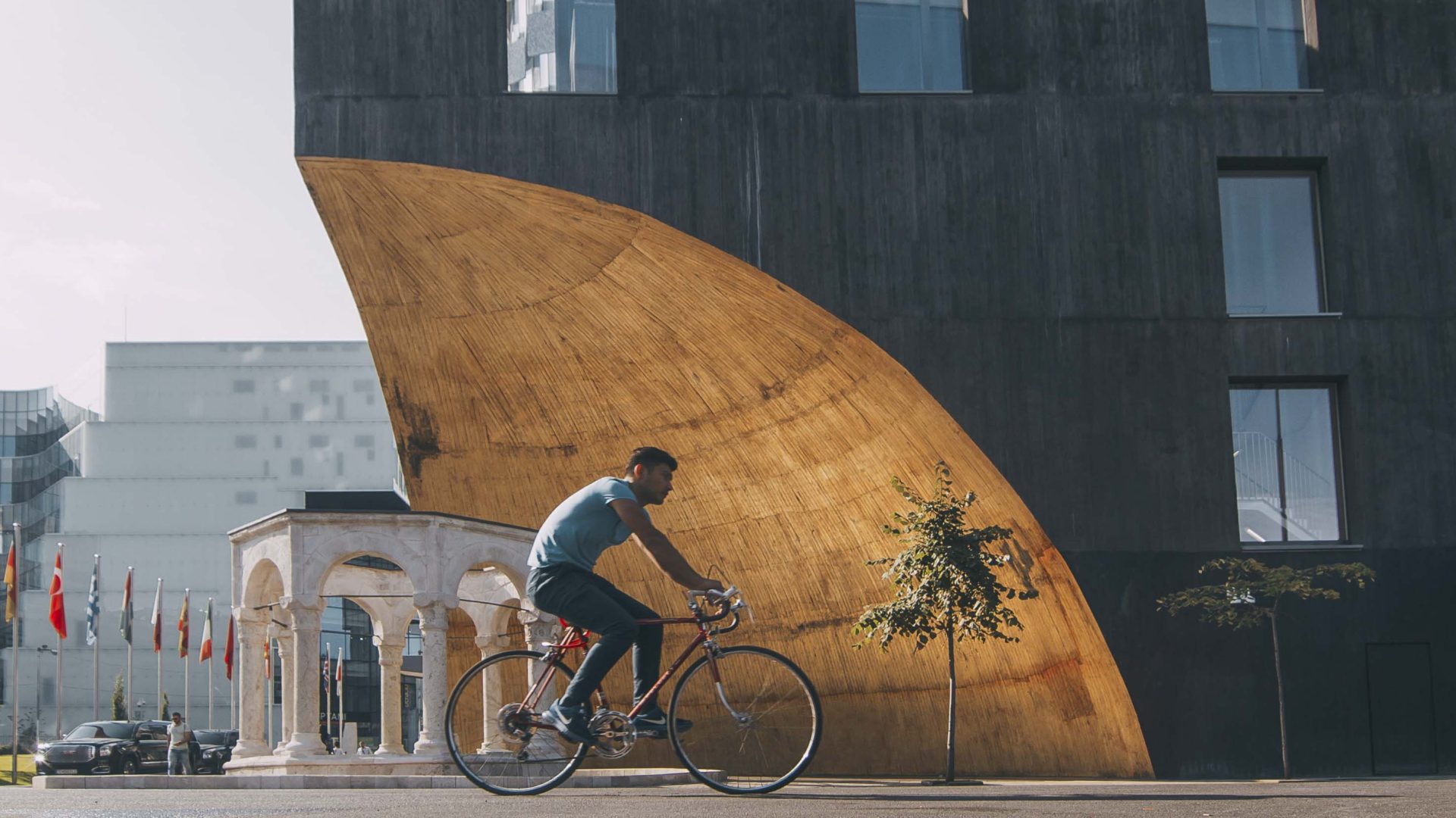 A man rides his bike past a curved shaped building.