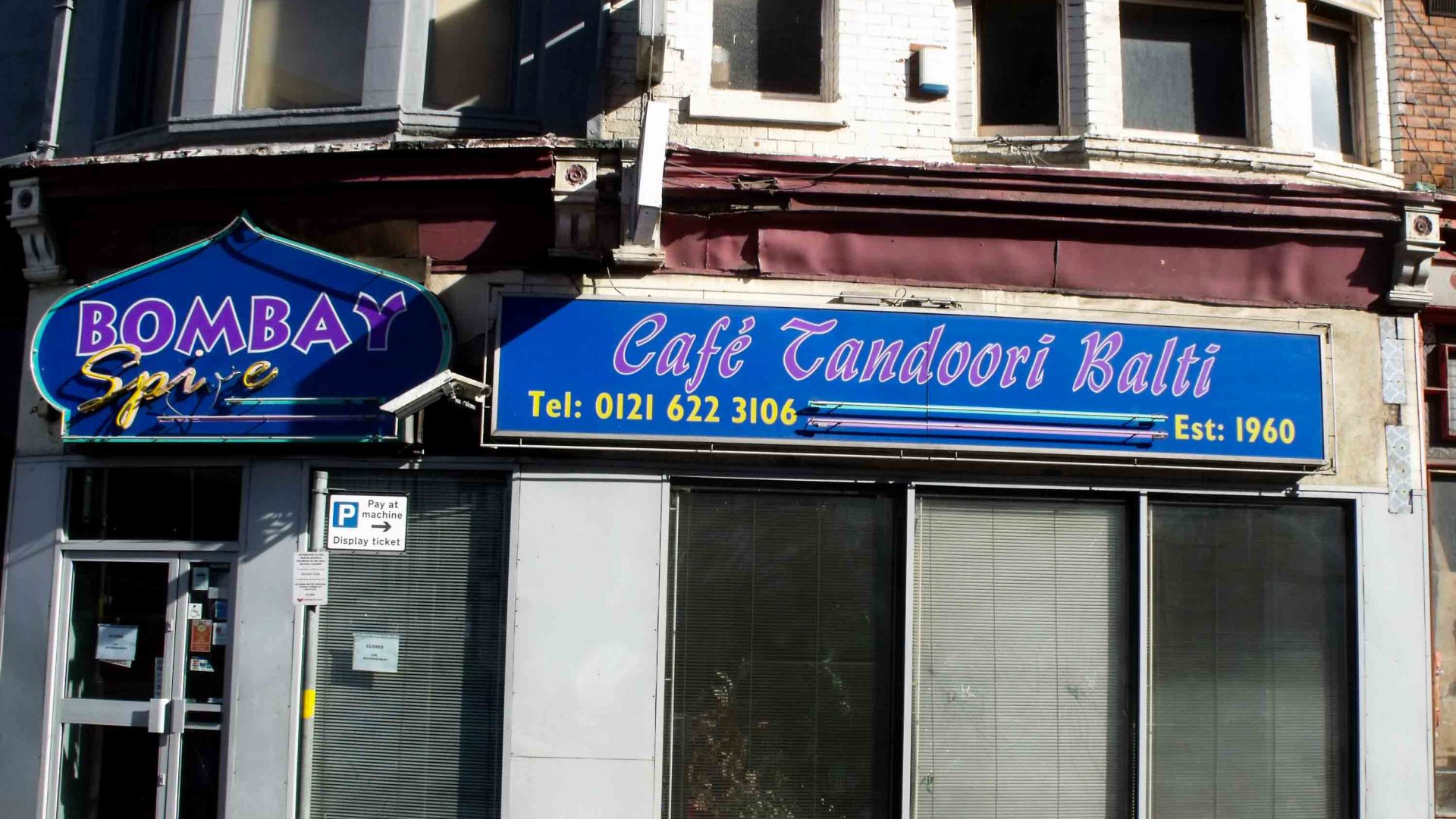The front of a restaurant with blue signage that says 'Cafe Tandoori Balti).