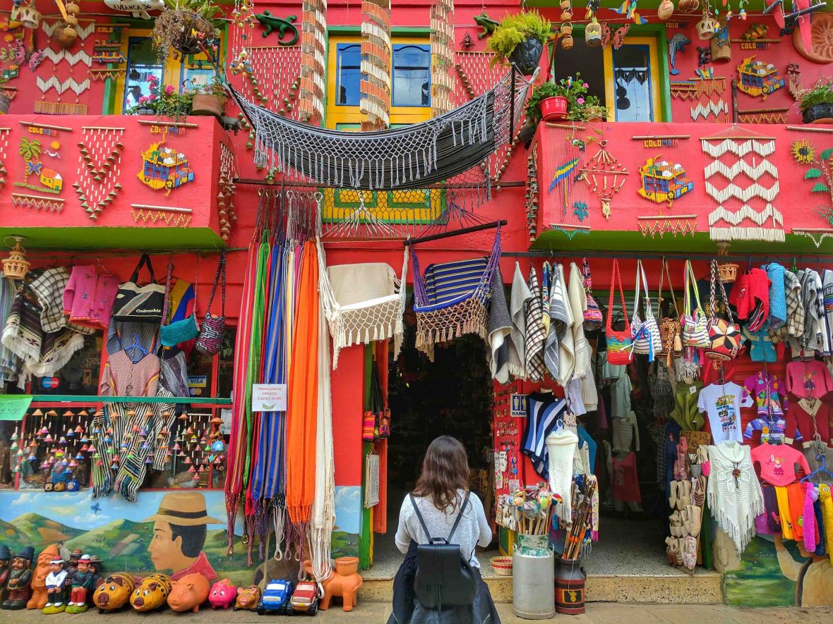 A woman enters a store in Medellin in Colombia. Ut is painted red and has lots of colorful artefacts and handicrafts hanging from the walls.