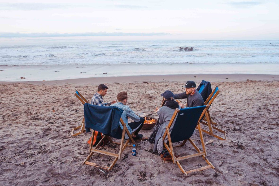 Young men sit around on chairs on a beach.