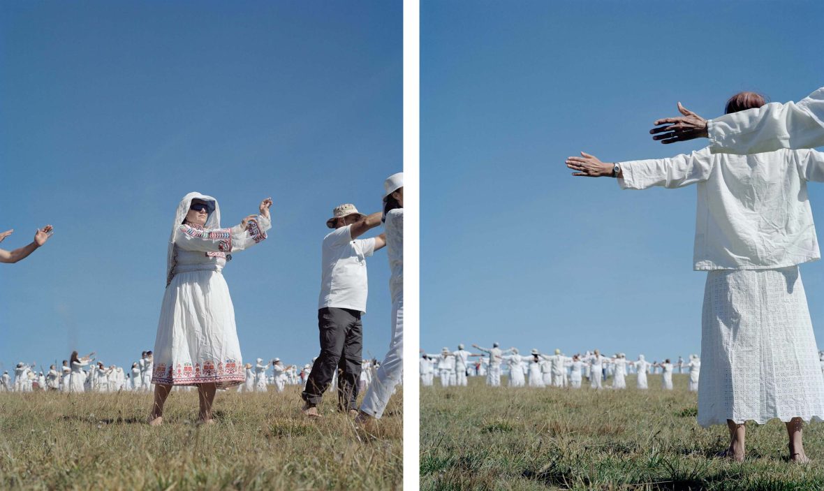 People dressed in white dance on a green hill.