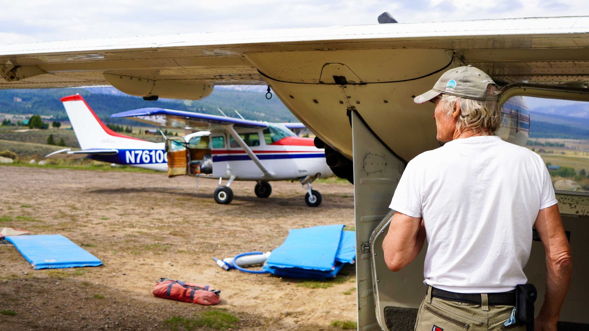 A man seen from behind stands alongside an airplane. There is another airplane in the distance.