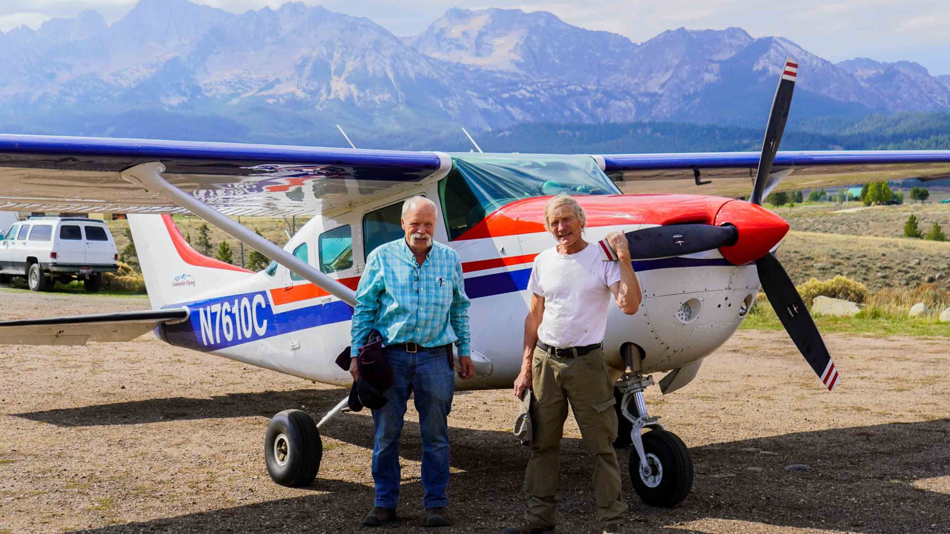 Two men stand in front of a small airplane.