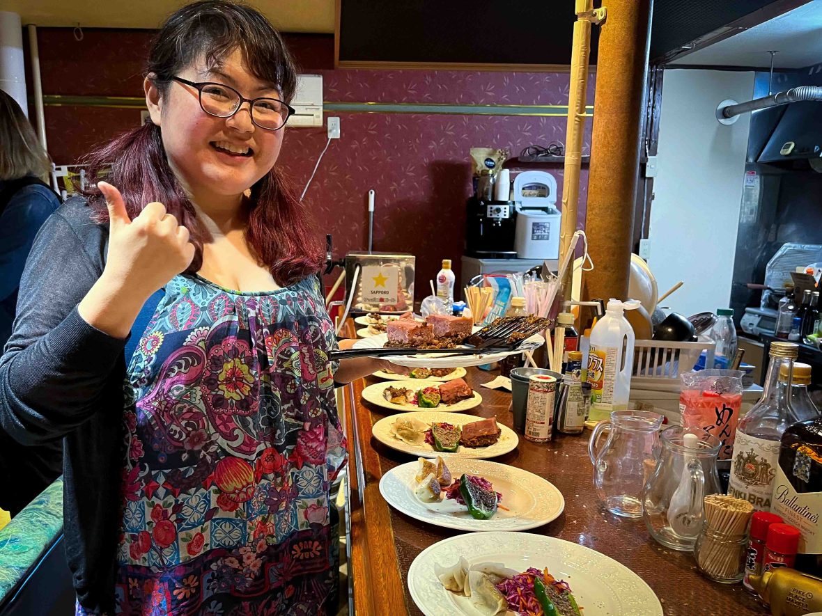 A woman smiles alongside plates of food.