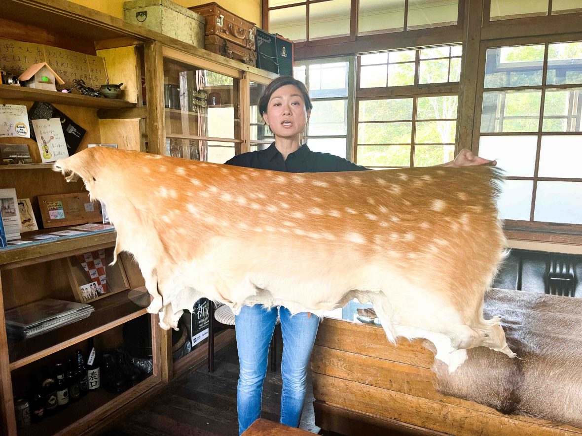 A woman holds up a deer hide.