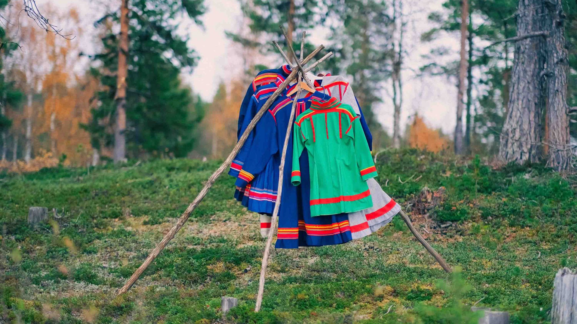 Sami designer dresses hang on a rack in the forest.