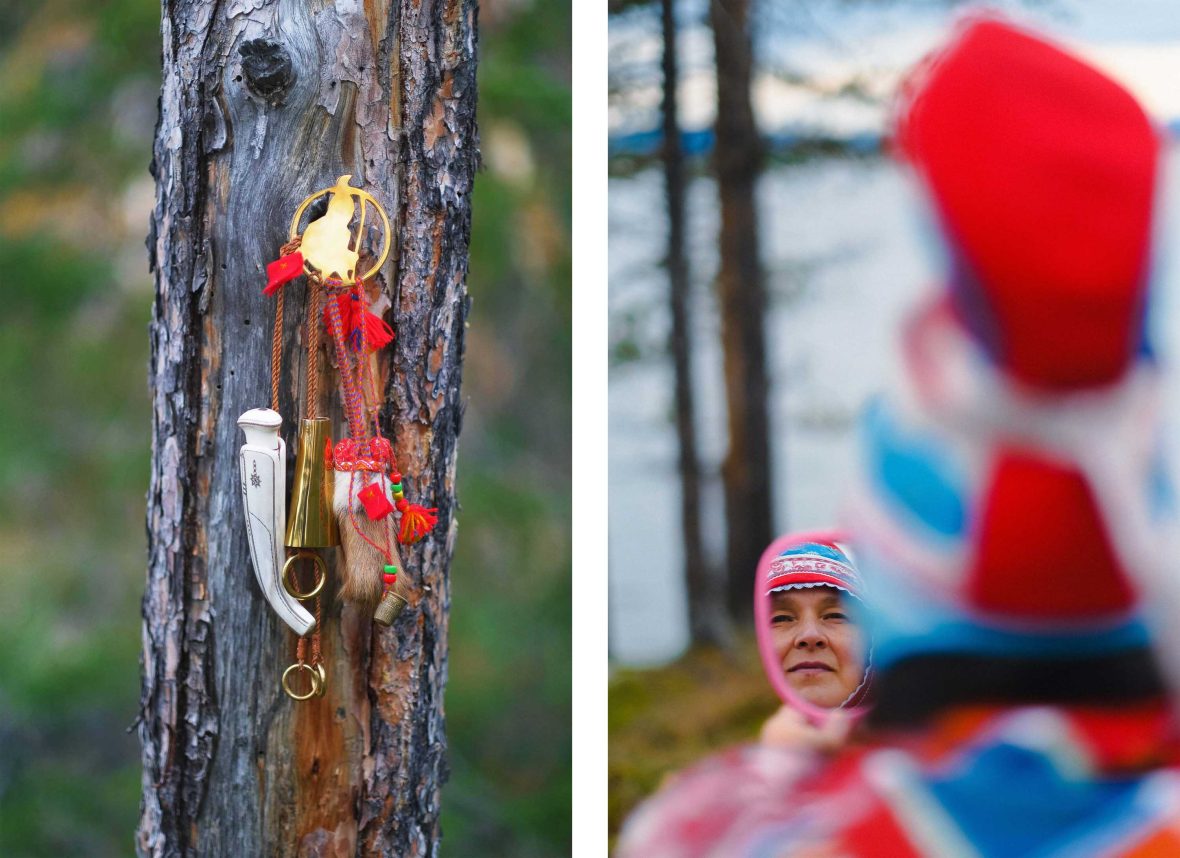 A tree with a collection of Sami items hanging from it, and a Sami woman looks into a small mirror.
