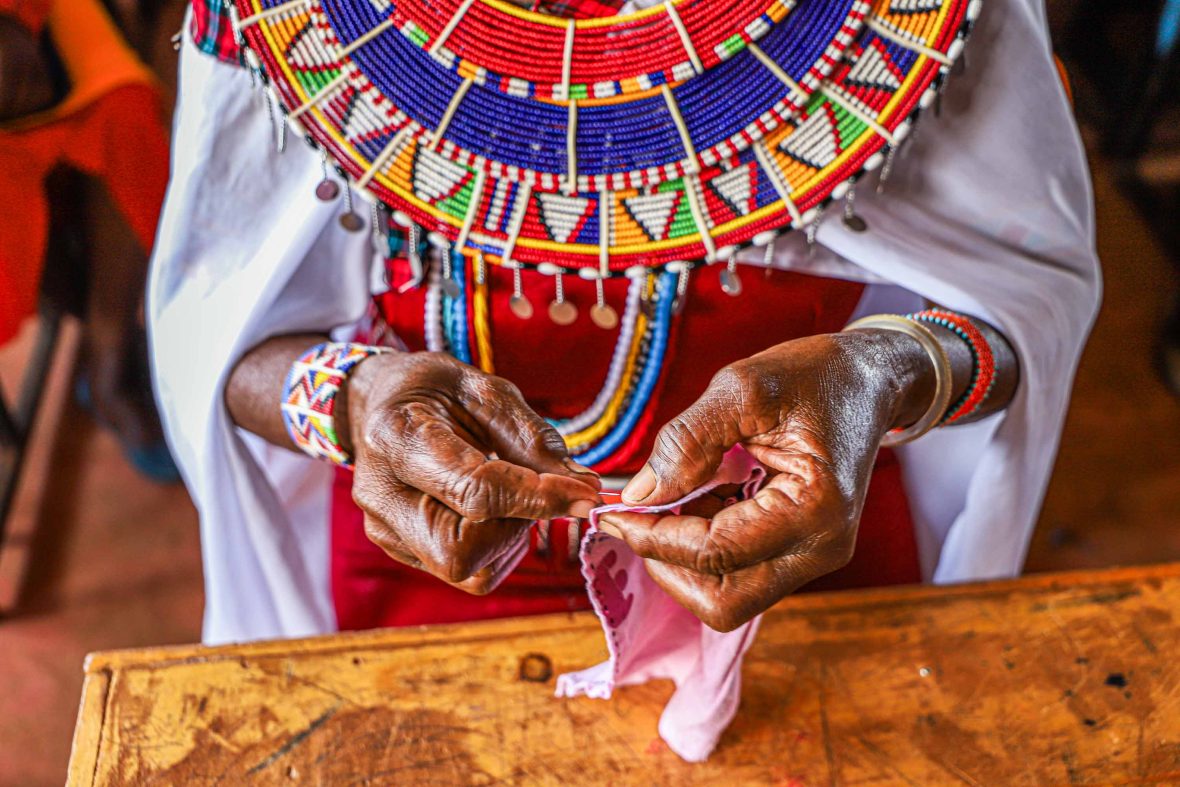 A close up of a Massai womans hands sewing a piece of fabric.