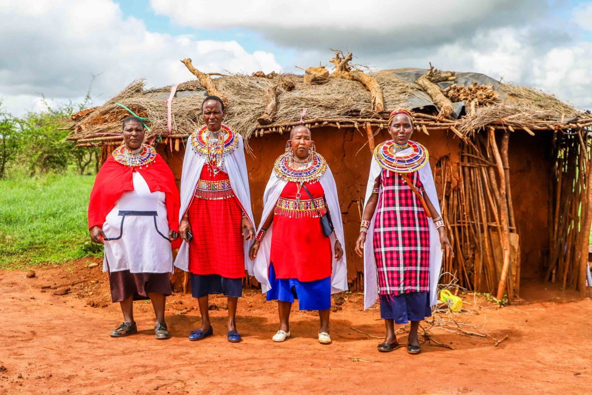 Massai women stand in front of a hut.