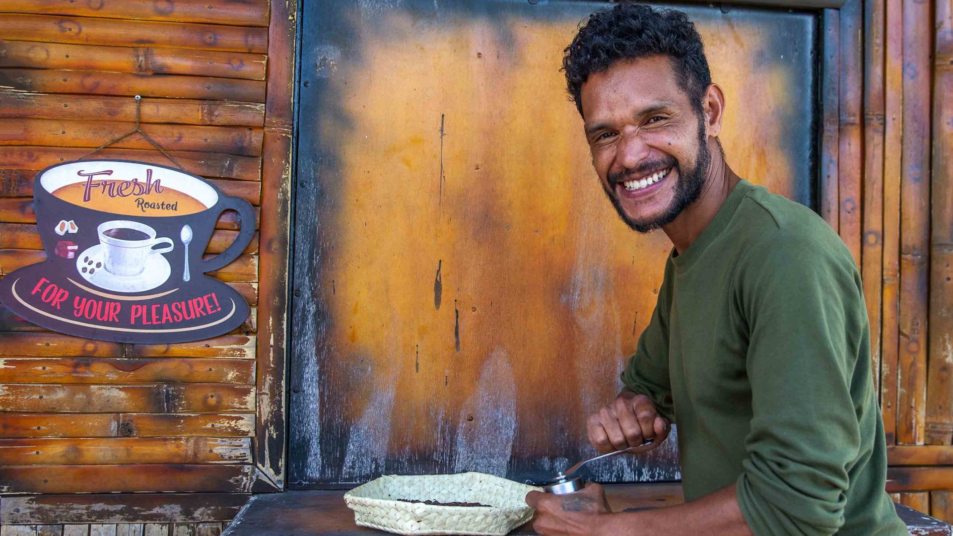 A man holds a plate of coffee beans and smiles to camera. Timor Leste Timor-Leste grows both arabica and robusta beans.
